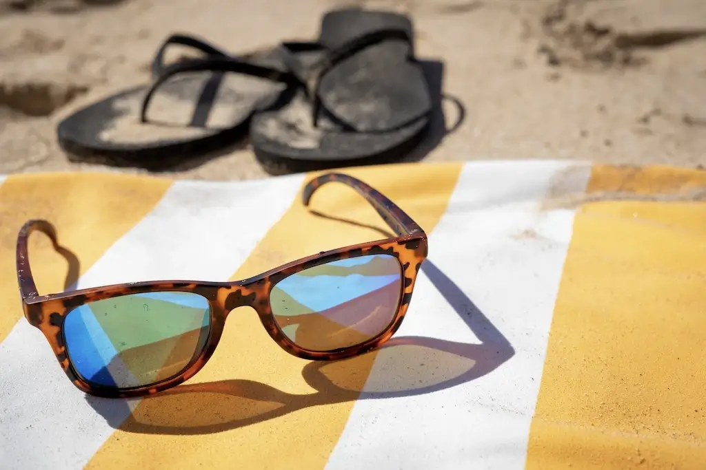 Sunglasses, flip-flops and a towel on a beach.