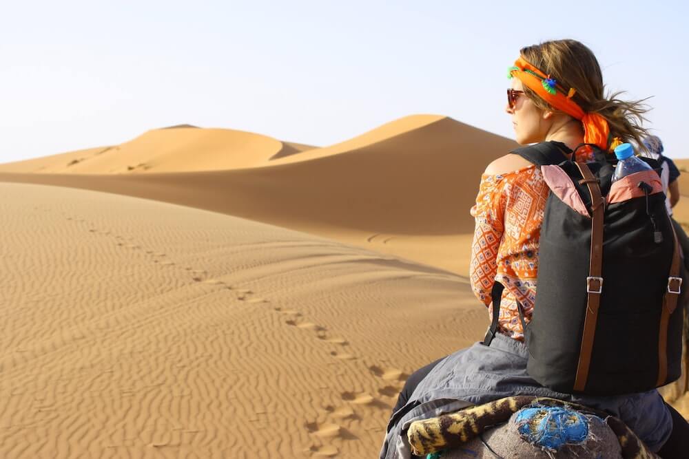 A female solo traveller rides a camel through the Sahara Desert.