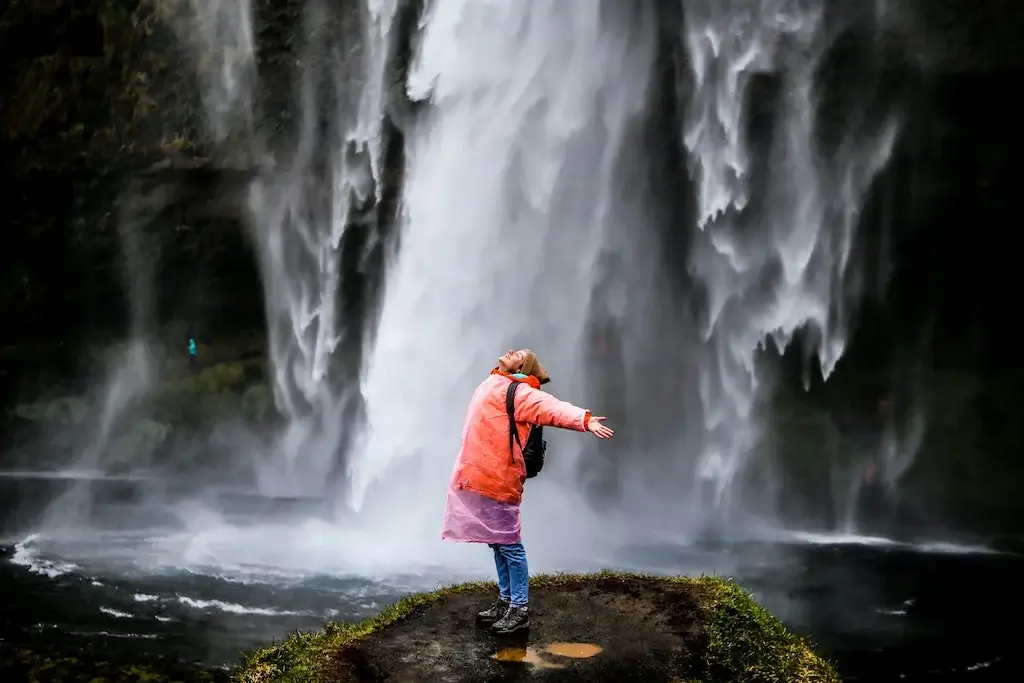 A woman in a raincoat stands underneath a waterfall.
