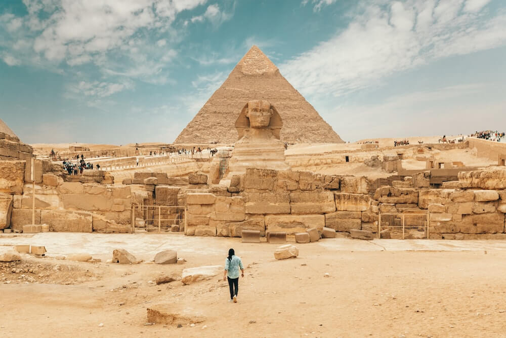 A male solo traveller walks towards the Sphinx and the Pyramids in Giza, Egypt.