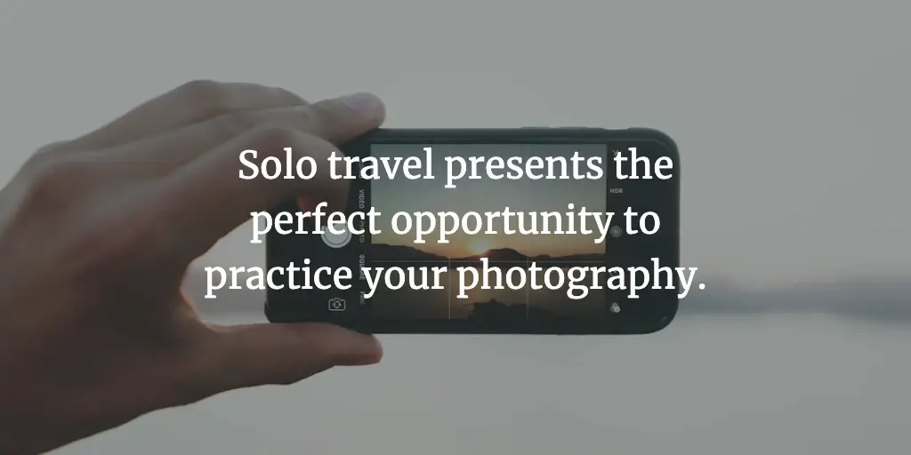 A smartphone camera taking a photo of a sunset. The text reads, 'Solo travel presents the perfect opportunity to practice your photography.'