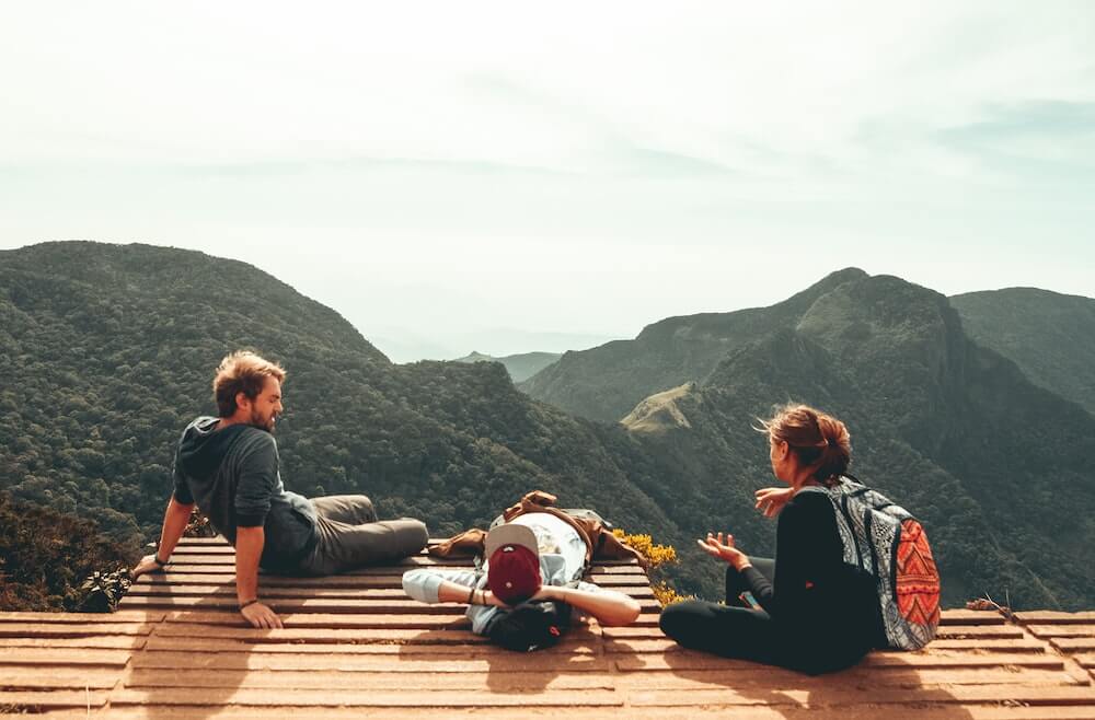 Three travel friends sit at a mountain lookout.