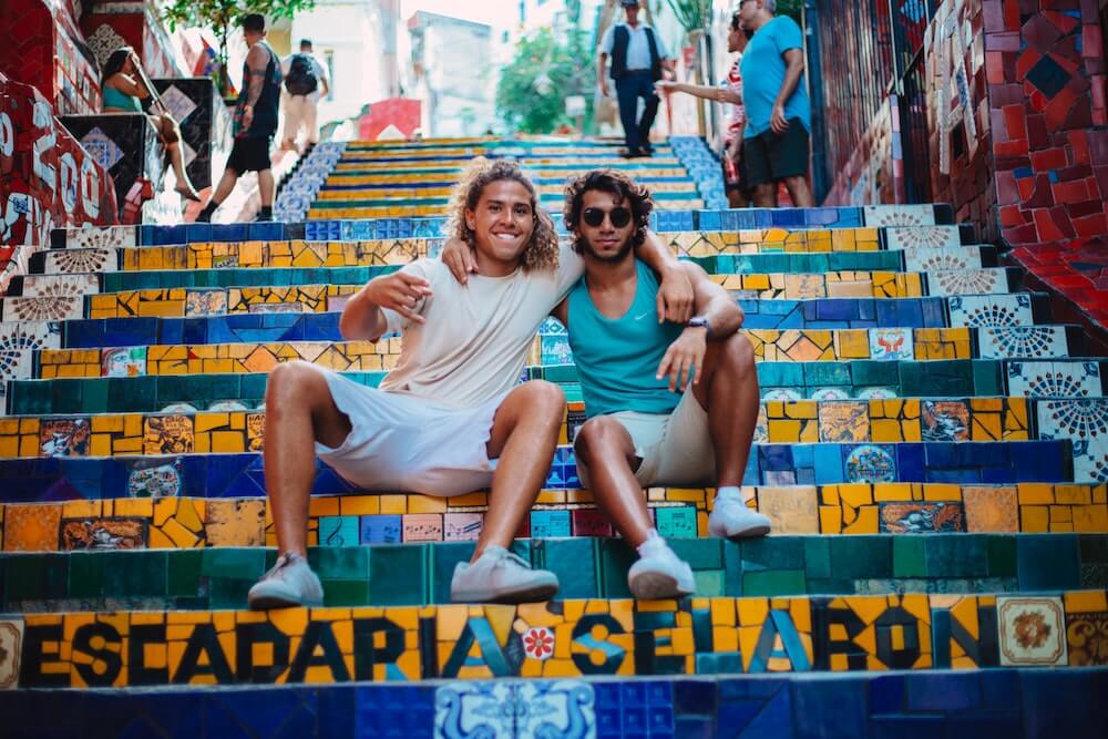 Two male travel friends sit on some stairs together in South America.
