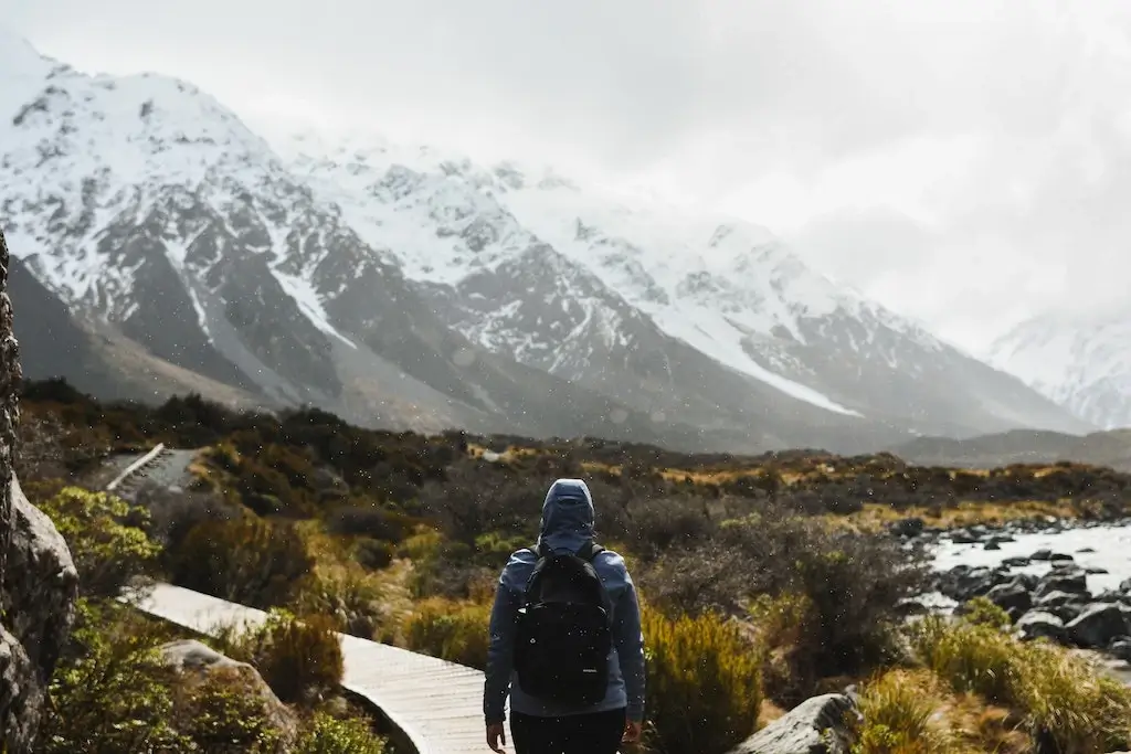 A male solo traveller hiking Mount Cook National Park, with a jacket and backpack in the rain.