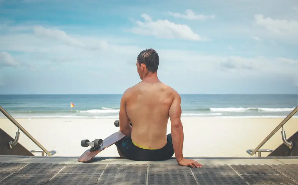 A male solo travellers in Australia on the beach with a skateboard.