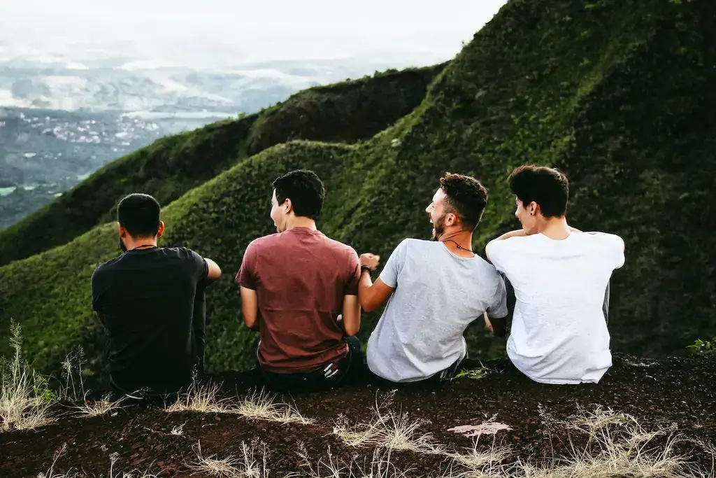 Four male travel buddies laugh overlooking a valley
