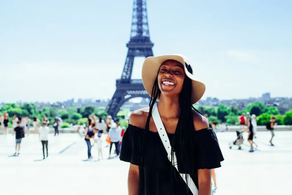 A solo travel woman smiling in front of the Eiffel Tower, Paris, France.