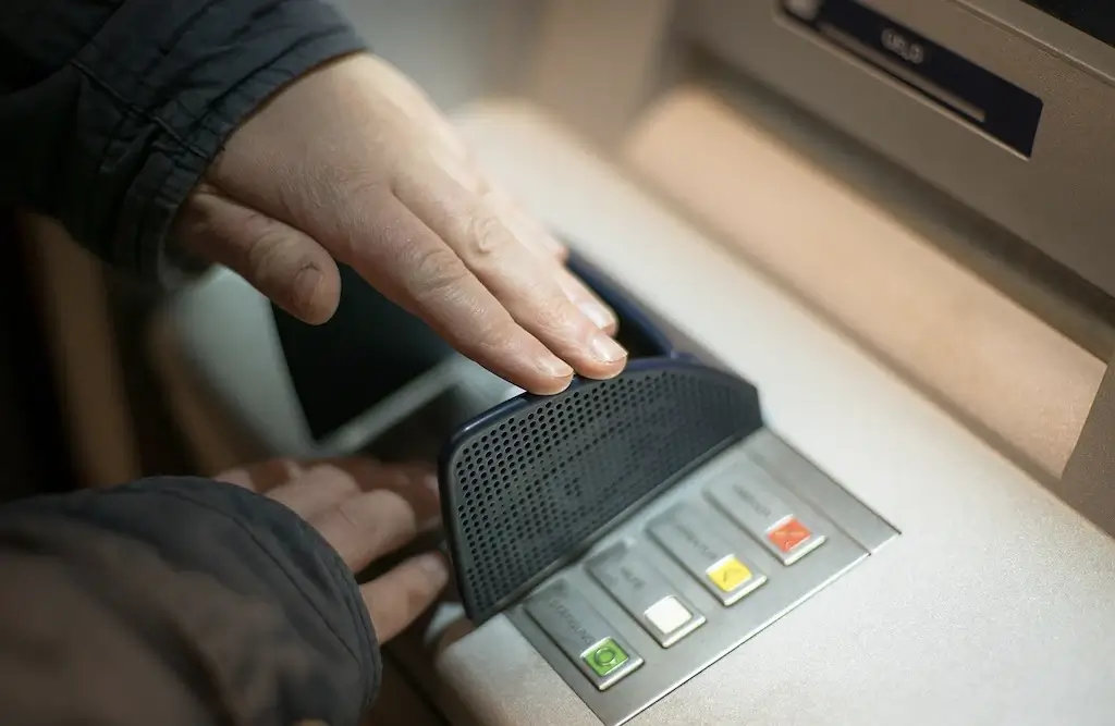 A person covering their pin code at an ATM to avoid fraud and theft.