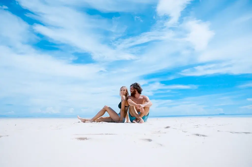 Travel couple sitting together on a beach.