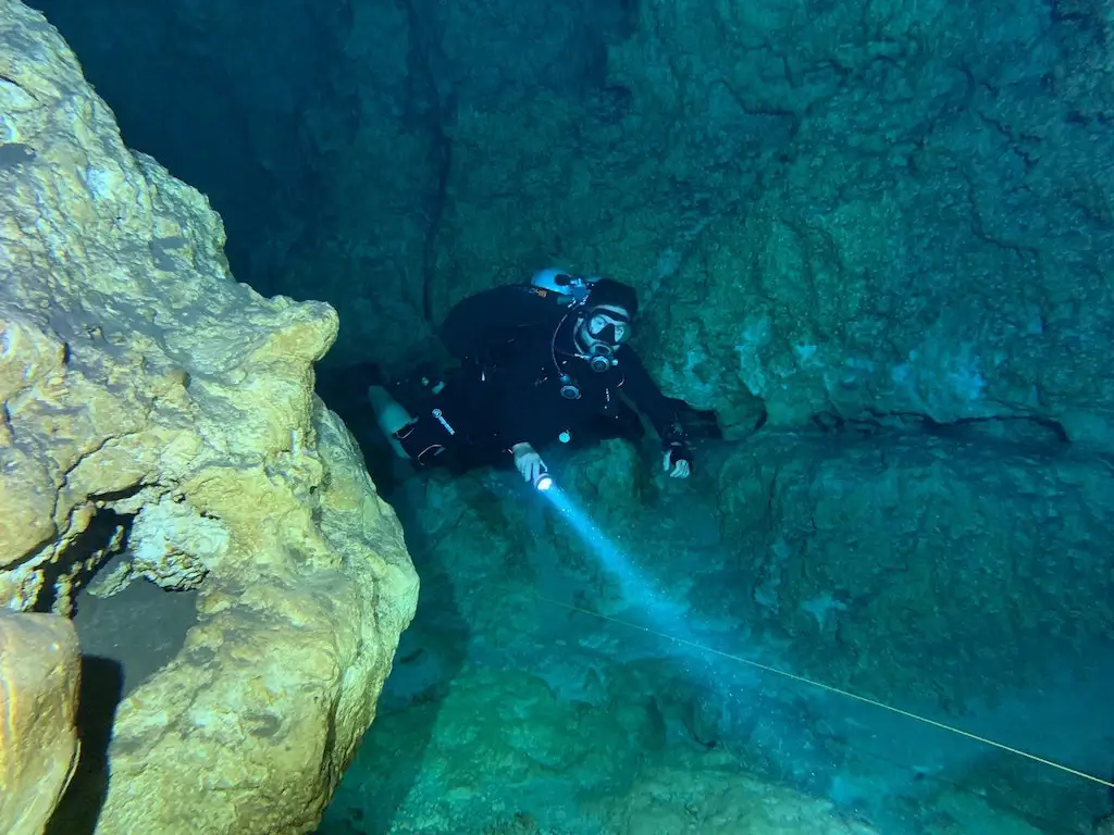 Cave diver using a rope and torch to navigate.