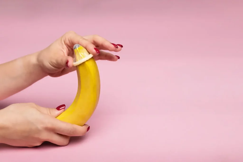 Female hand rolling a condom onto a banana.