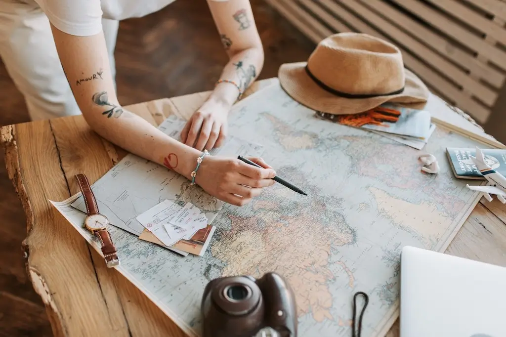 Tattooed woman planning travel on a map with camera.