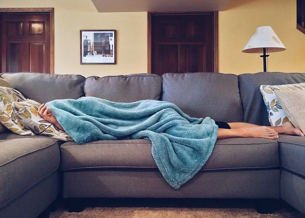 Woman sleeping on a couch covered in blanket.
