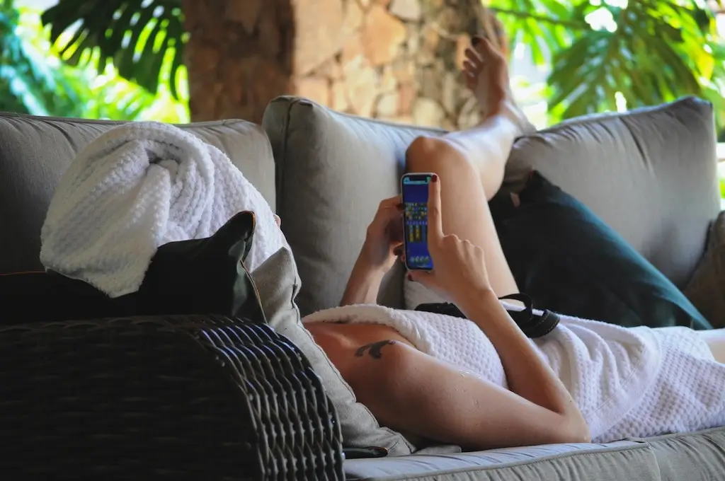 Woman wearing a towel lying down and messaging on her phone.