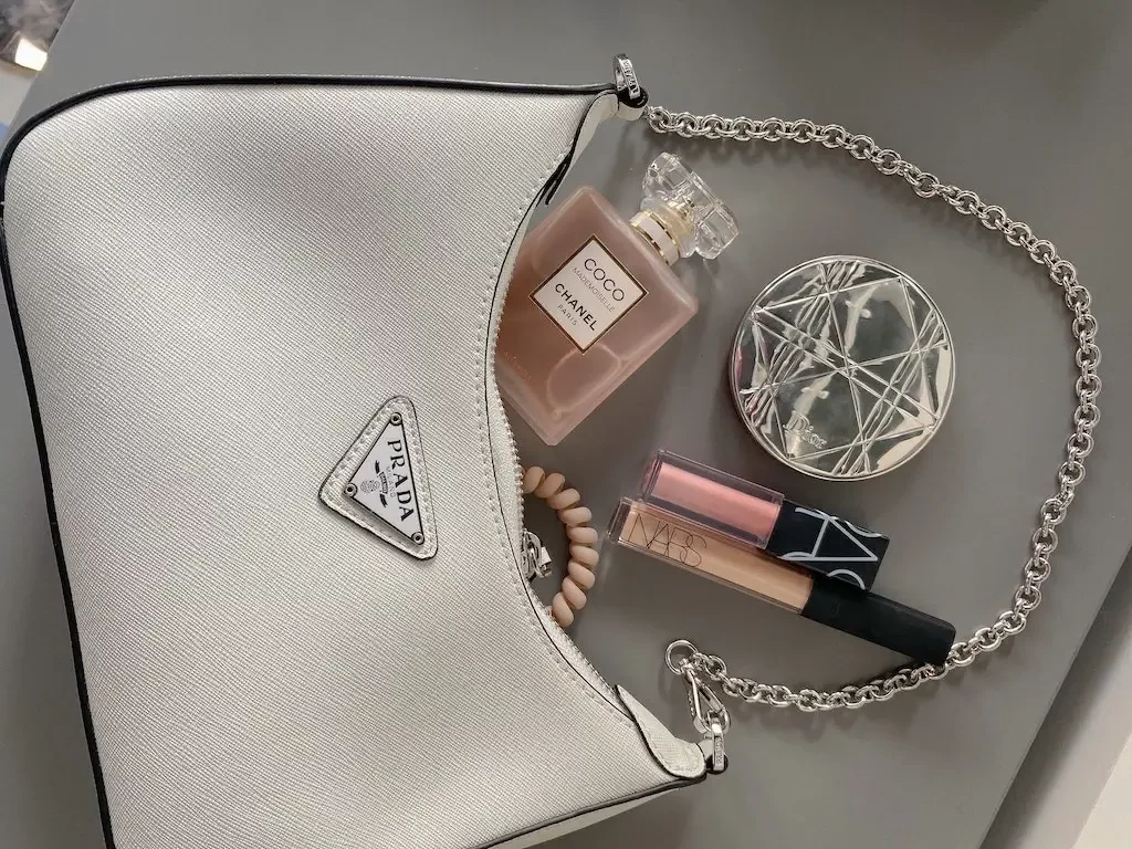 Prada purse spilling with Chanel perfume and lipstick.
