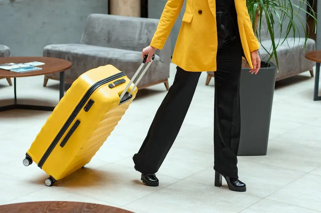 Solo female traveller wearing a yellow coat and pulling a yellow suitcase.