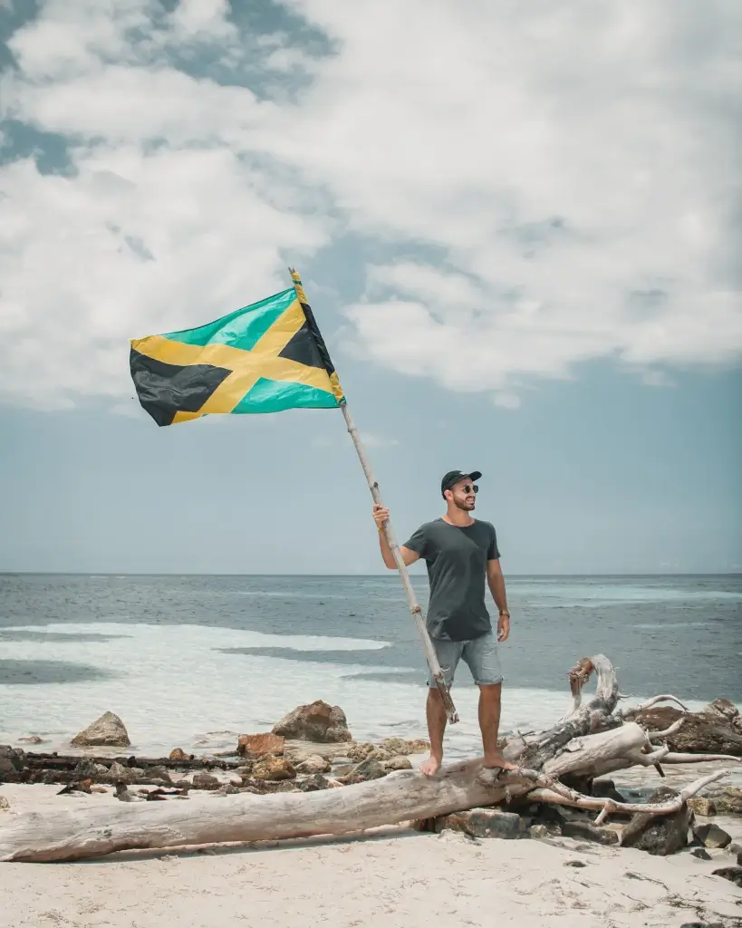 Male solo traveller with a Jamaican flag on beach in Jamaica. 