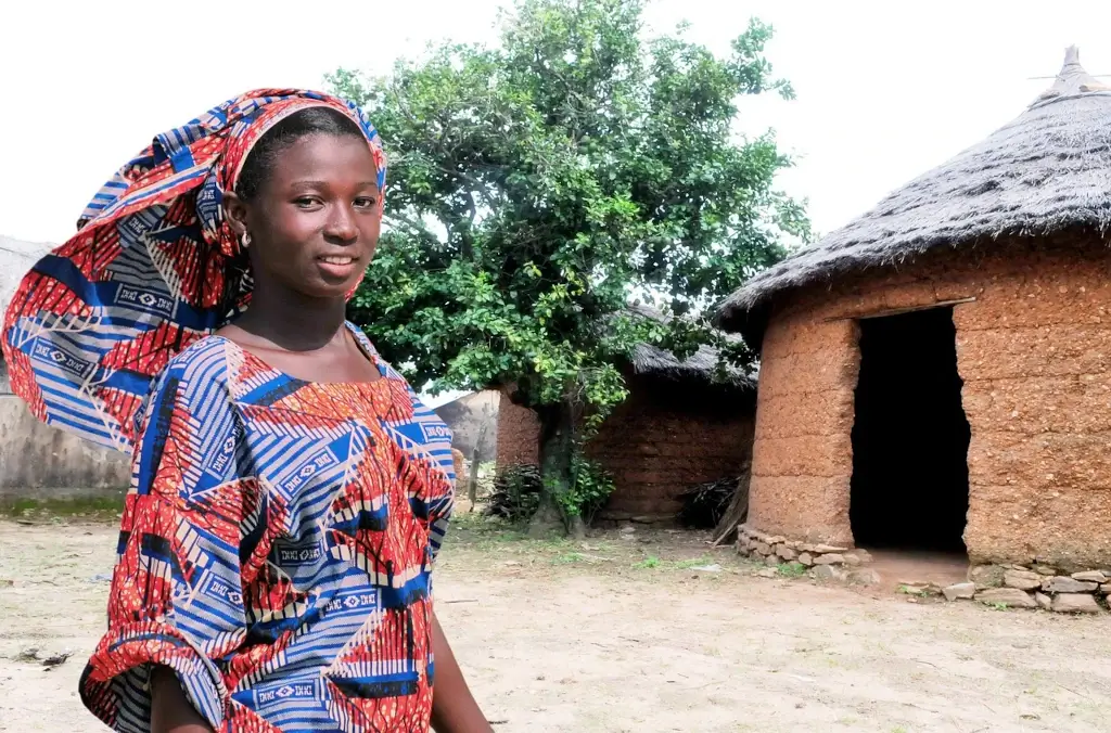 A woman dressed in colourful traditional clothing outside a mud house in Togo. 